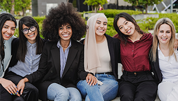 group of multicultural young women sitting outside and smiling at camera